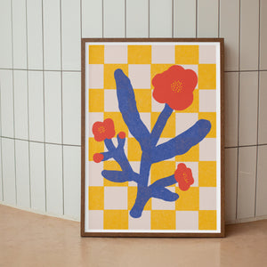 Framed artwork with blue branch and red flowers on a yellow and white checkered background, leaning against a tiled wall.