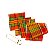 Set of colorful Merry Madras cocktail napkins fanned out on a white background beside a brass bottle opener, showing the bold red, green, and yellow plaid pattern.