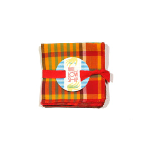Four Merry Madras cocktail napkins neatly folded and tied with a red ribbon, finished with the Willow Ship round tag, ready for gifting.