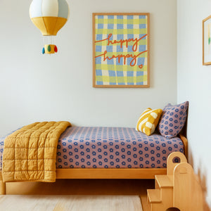 Children's bedroom with a bed, yellow blanket, and colorful optimistic wall art.