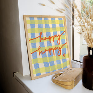 Framed checkered art print with 'happy happy' text on a shelf next to a vase.