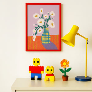 Colorful nursery scene with plastic LEGO toys, a yellow lamp and vibrant artwork featuring white blooms, a textural vase and lavender background.