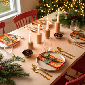Festive dining table featuring Merry Madras dinner napkins at each place setting, with warm candlelight and holiday lights in the background.